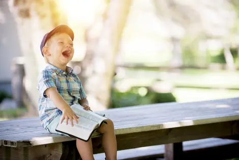 Symbolfoto: Ein kleiner Bub sitzt auf einer Ban und blättert in einem Buch.